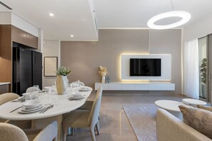 A modern dining area with a round table set for four, a flat-screen TV mounted on the wall, and a minimalist design with neutral colors.