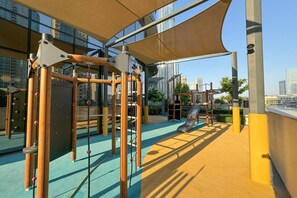 An outdoor playground with climbing structures and a slide, set against a backdrop of high-rise buildings. - Majestic 2 BDR with Burj Khalifa and Fountain View (Dubai)