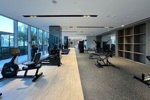 Un gimnasio moderno con máquinas de cardio, estaciones de pesas y un amplio ventanal con vistas a la ciudad.