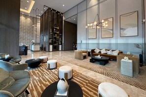 A modern lobby with a mix of seating areas, a reception desk, and a staircase leading to upper floors.