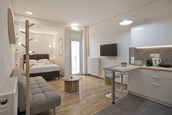 Una camera d'albergo moderna con un letto, un divano, un piccolo tavolino rotondo, angolo cottura e una TV a parete.