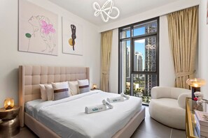 Una habitación de hotel con una cama grande, una zona de estar, obras de arte en las paredes y vistas a la ciudad desde la ventana.