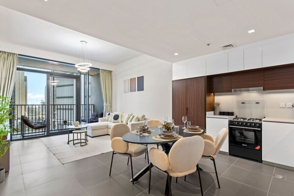 A modern apartment with a dining area, kitchen, and balcony with a city view.