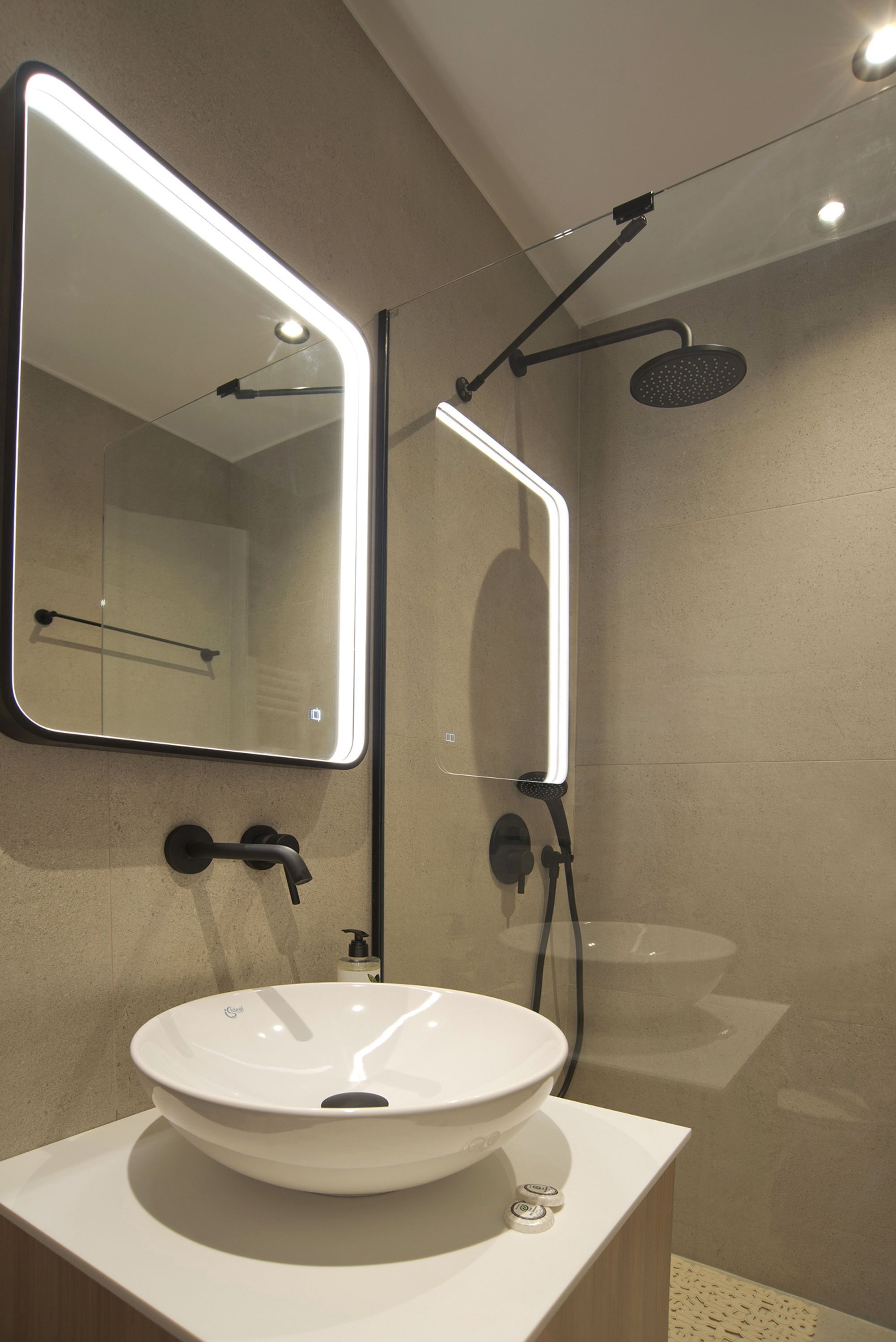 A modern bathroom with a round white sink, a mirror with integrated lighting, and a handheld showerhead.