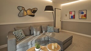 A modern living room with a grey sectional sofa, a floor lamp, abstract wall art, and a small table with candles and a plant. - Urban Allure in Athina (Athens)