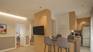 A modern kitchen with a central island, bar stools, a flat-screen TV, and a decorative clock on the wall. - Urban Allure in Athina (Athens)