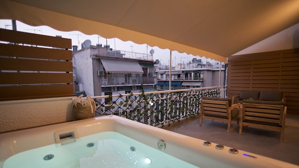 A rooftop terrace with a hot tub, wooden seating, and a view of surrounding buildings. - Urban Allure in Athina (Athens)