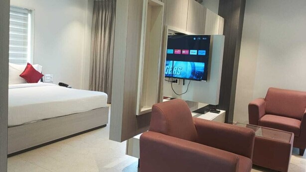 A modern hotel room with a bed, a TV, and two armchairs. - HOTEL RAMKRISHNA PALACE (Bijapur)