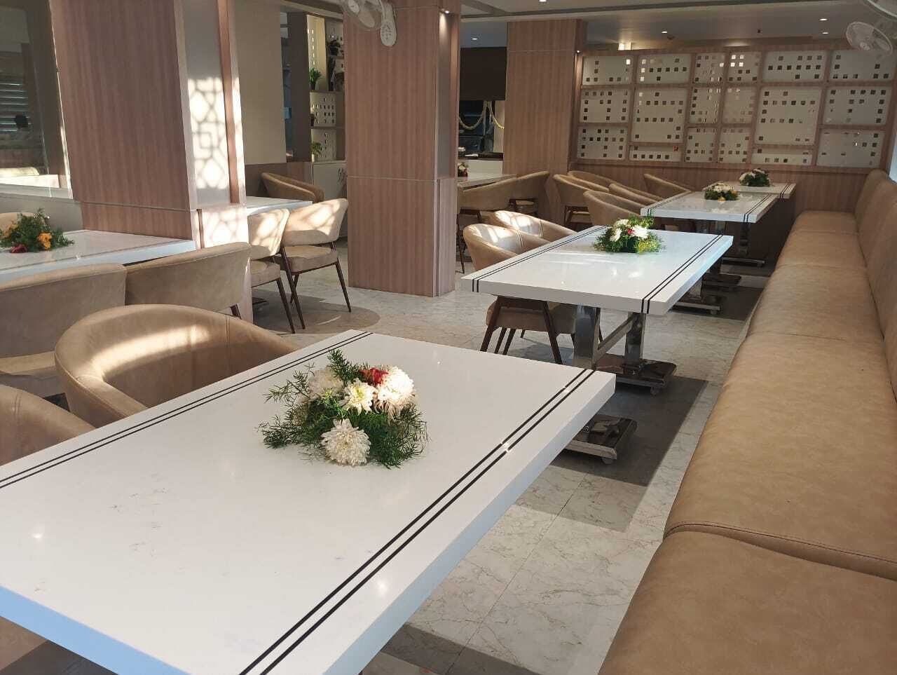 A modern dining area with white tables and beige chairs, featuring a central floral arrangement.