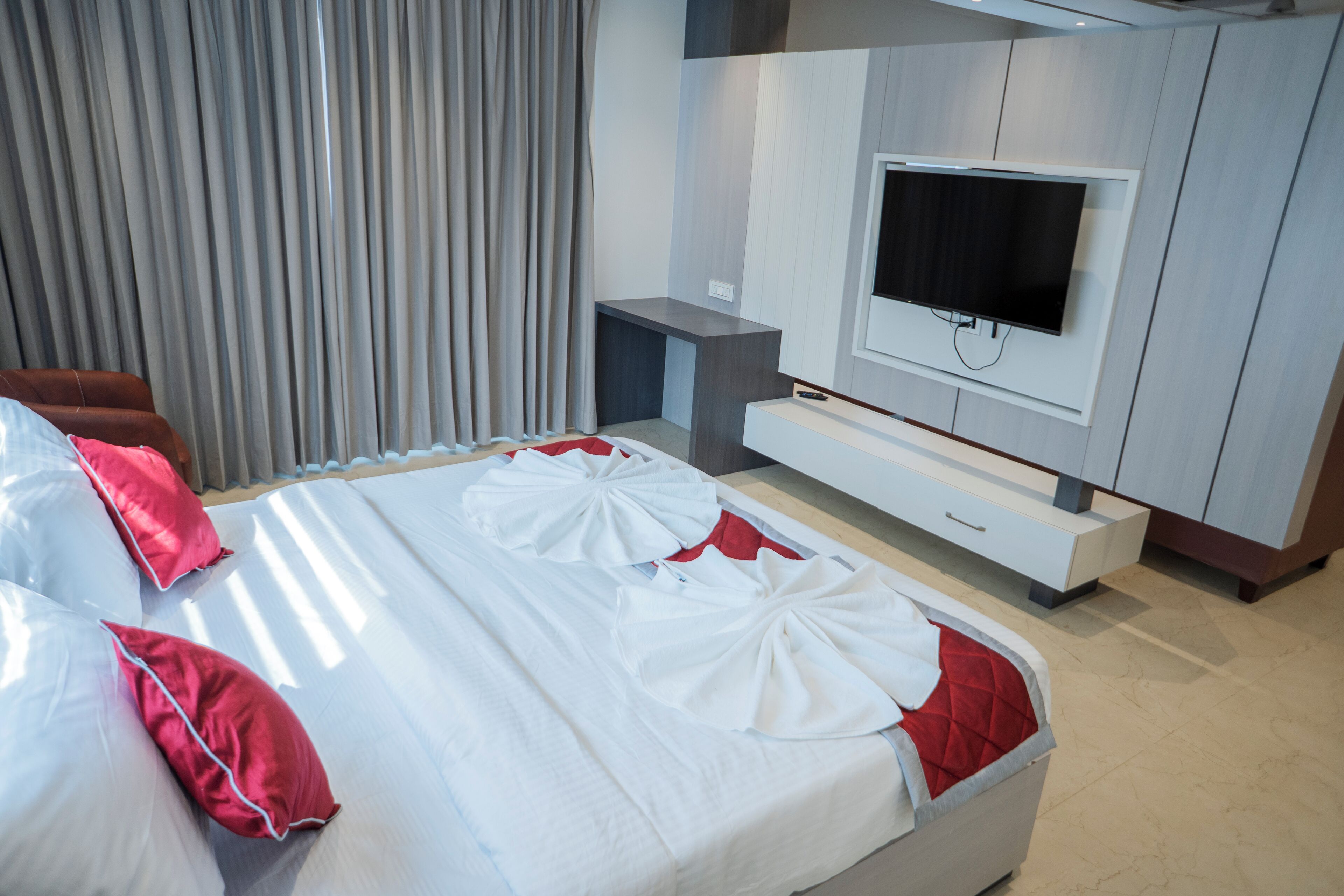 A modern hotel room with a large bed, a flat-screen TV, and a built-in bench.