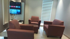 A living room with three red armchairs, a flat-screen TV, and a window with blinds. - HOTEL RAMKRISHNA PALACE (Bijapur)