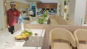 A modern restaurant interior with a long counter, cushioned seating, and a glass partition. - HOTEL RAMKRISHNA PALACE (Bijapur)