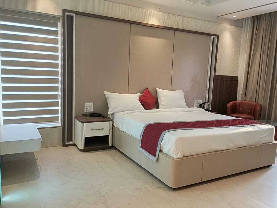 A modern bedroom with a large bed, a bedside table, a chair, and a window with blinds.
