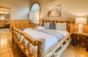 Ein Bett mit Holzrahmen, Blick auf einen Steg, eine Holzkommode und ein Fenster mit Vorhängen.