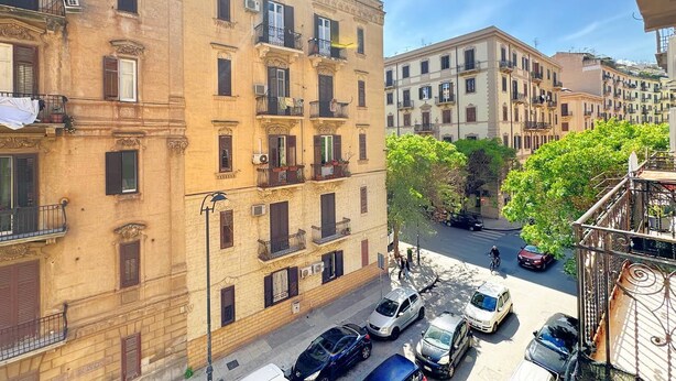 Une vue d’une rue dans un quartier résidentiel, avec des immeubles à plusieurs étages, des voitures garées et un cycliste sur la route.
