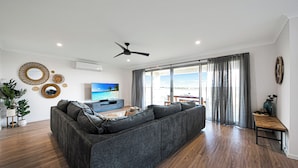 A modern living room with a large grey sectional sofa, a flat-screen TV, and a ceiling fan.