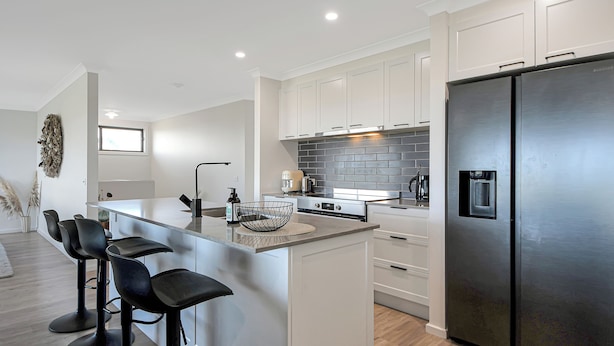 A modern kitchen with white cabinetry, a stainless steel refrigerator, and a central island with bar stools.