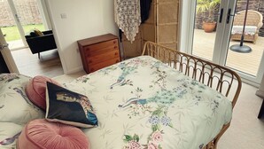 Un dormitorio con cama, cómoda de madera, silla de mimbre y vistas al exterior a través de una puerta corrediza de vidrio.