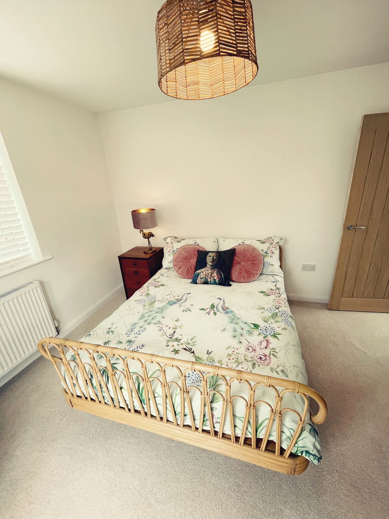 A bedroom with a bed, a bedside lamp, a wicker lamp, a wooden door, and a radiator.