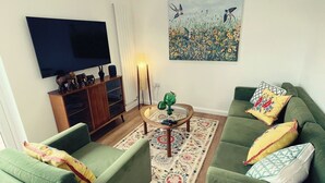 Una sala de estar con sofás verdes, una mesa de centro, un cuadro y un televisor en la pared.