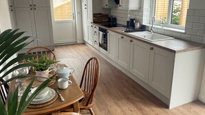 Una cocina moderna con armarios blancos, una mesa de comedor de madera y vistas al jardín a través de una ventana.