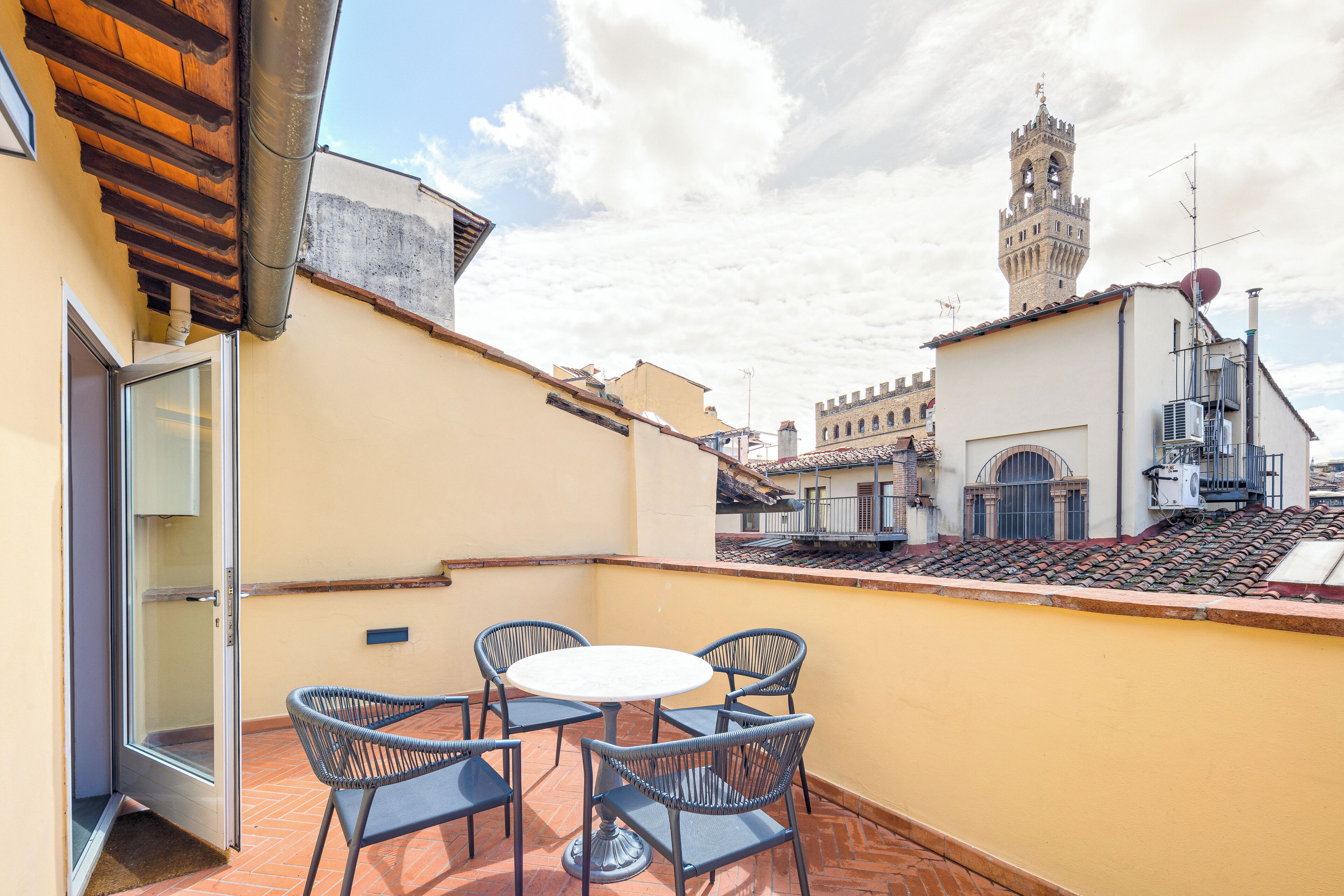 A rooftop terrace with a table and chairs, a door, and a view of a historic tower in the background.