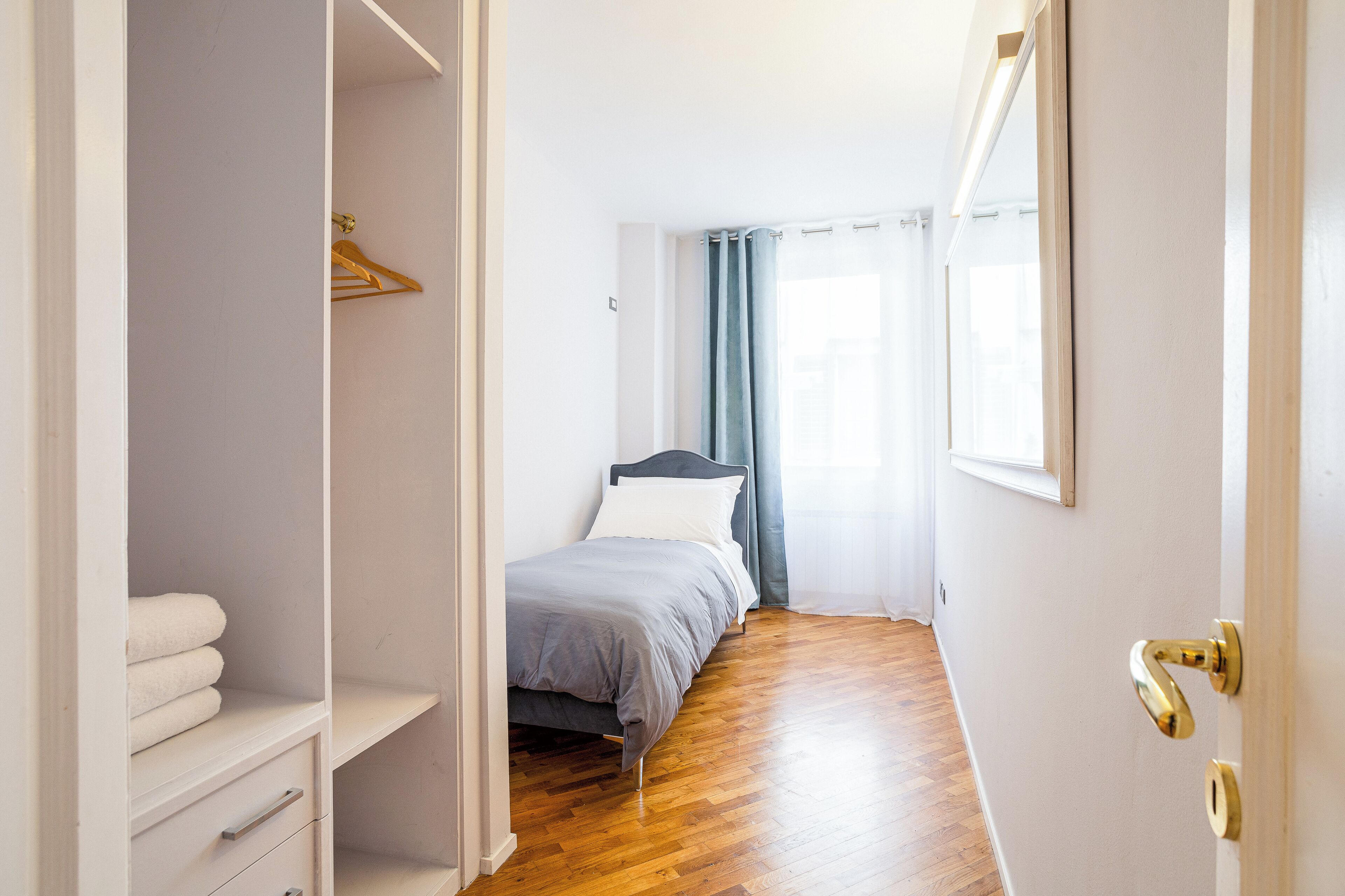 Un dormitorio con cama, armario y puerta con tirador de latón.