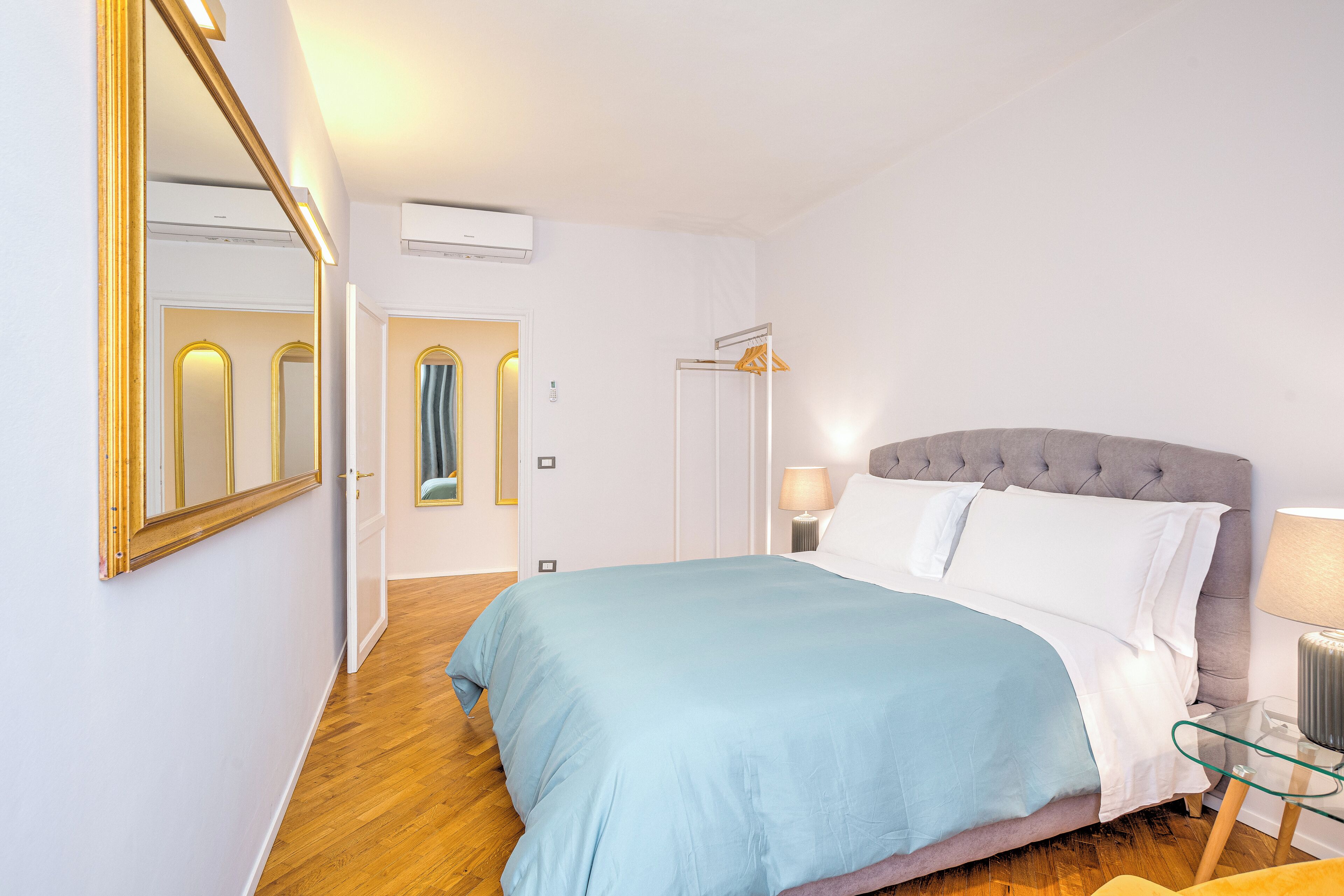 Un dormitorio con una cama grande, un espejo, un armario y una mesita de noche con una lámpara.