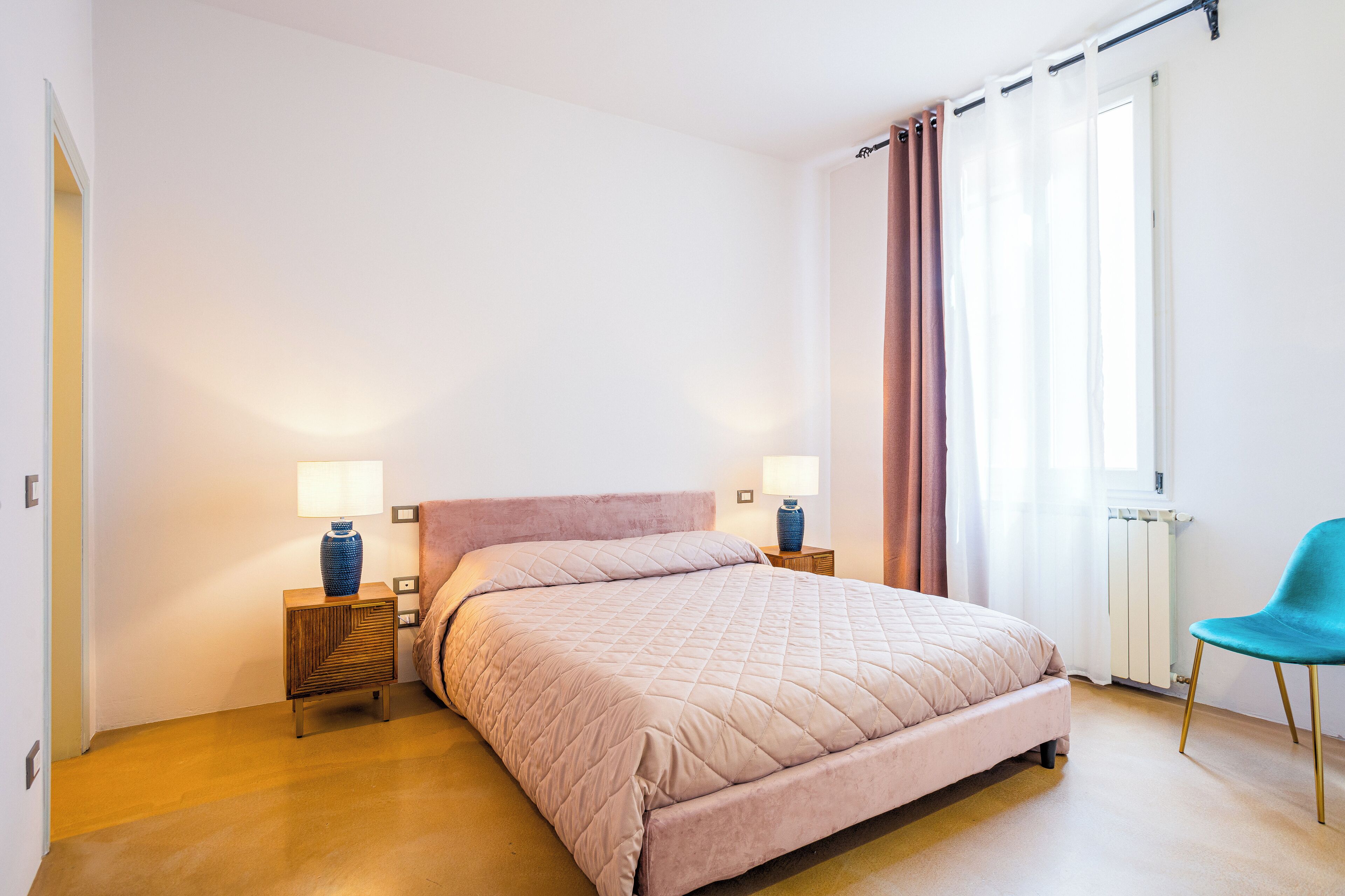 A bedroom with a bed, two bedside tables with lamps, a chair, and a window with curtains.