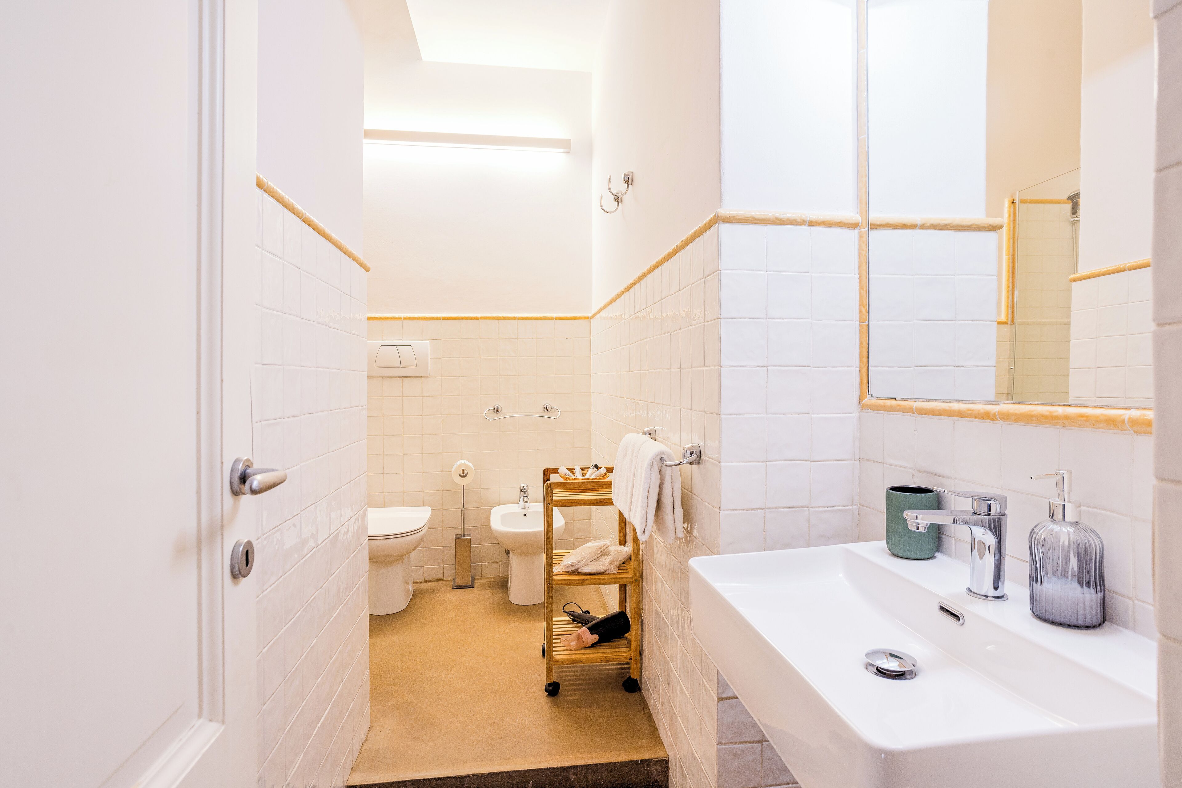 Ein Badezimmer mit weißem Waschbecken, einem Spiegel, einem Handtuchhalter und einer Toilette.