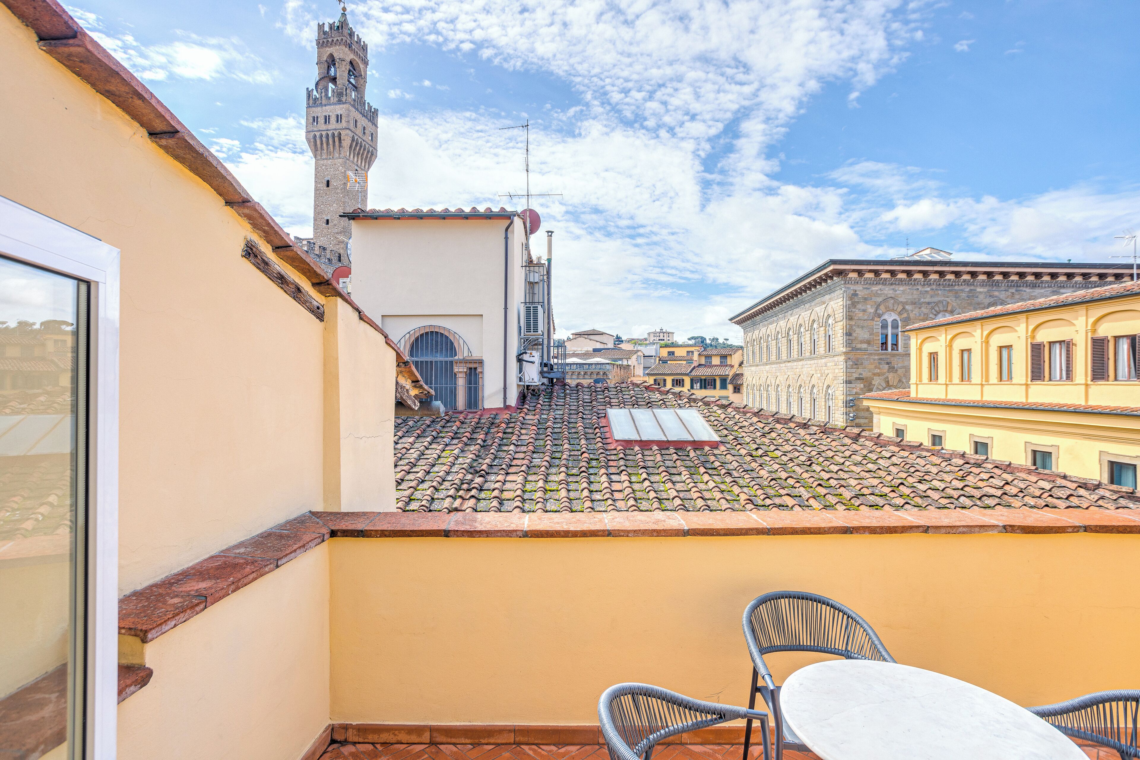 A rooftop terrace with a tiled roof, a table, and two chairs.