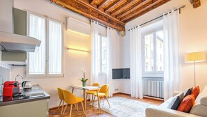 Une cuisine moderne avec une bouilloire rouge, une table à manger avec des chaises jaunes et un canapé avec des coussins orange.
