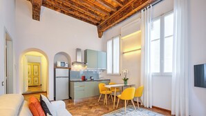 Un espace de vie compact comprenant un coin cuisine, un coin repas et un canapé avec des coussins.