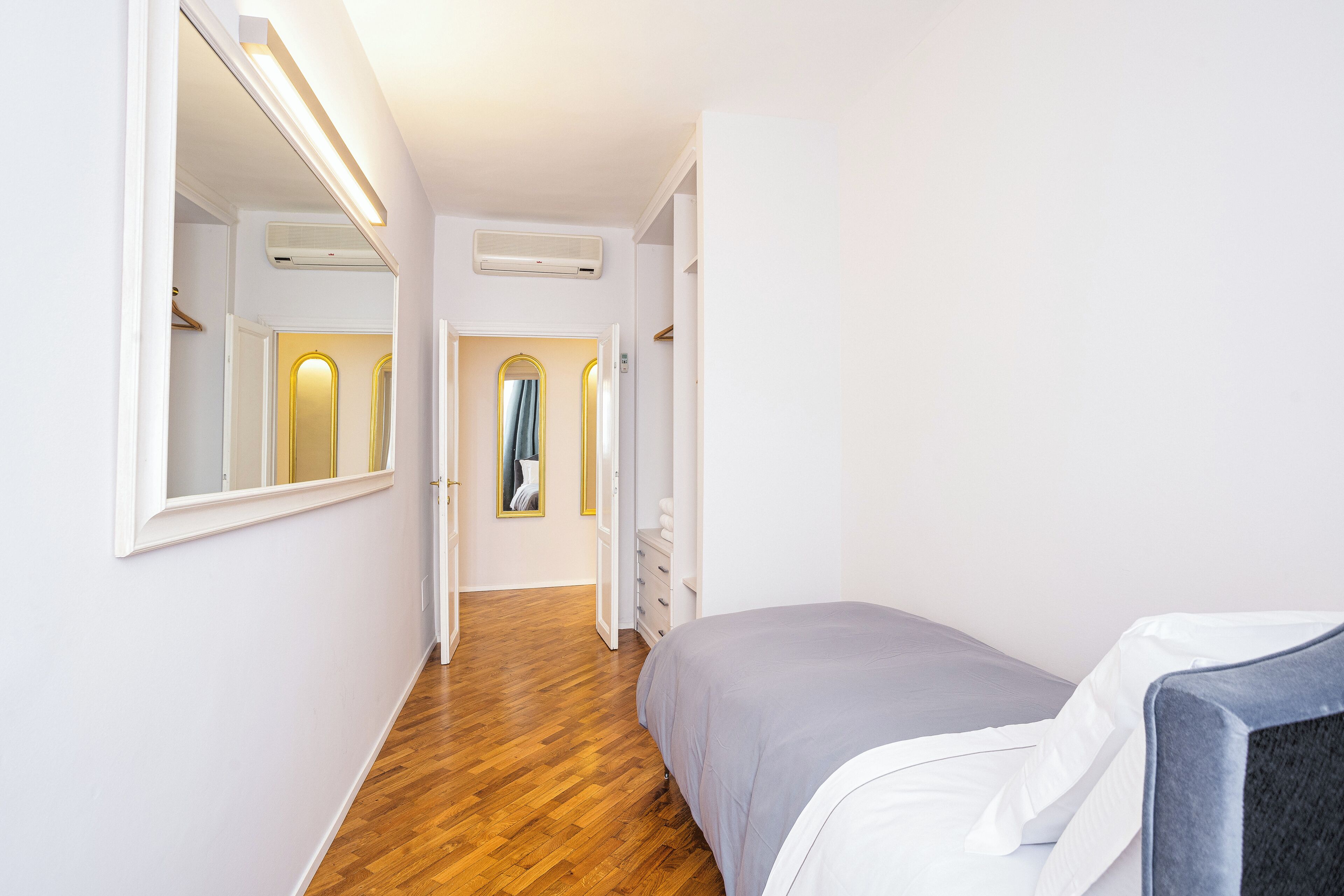 Un couloir étroit, doté d’un plancher en bois, mène à une chambre à coucher qui contient un lit et une chaise.