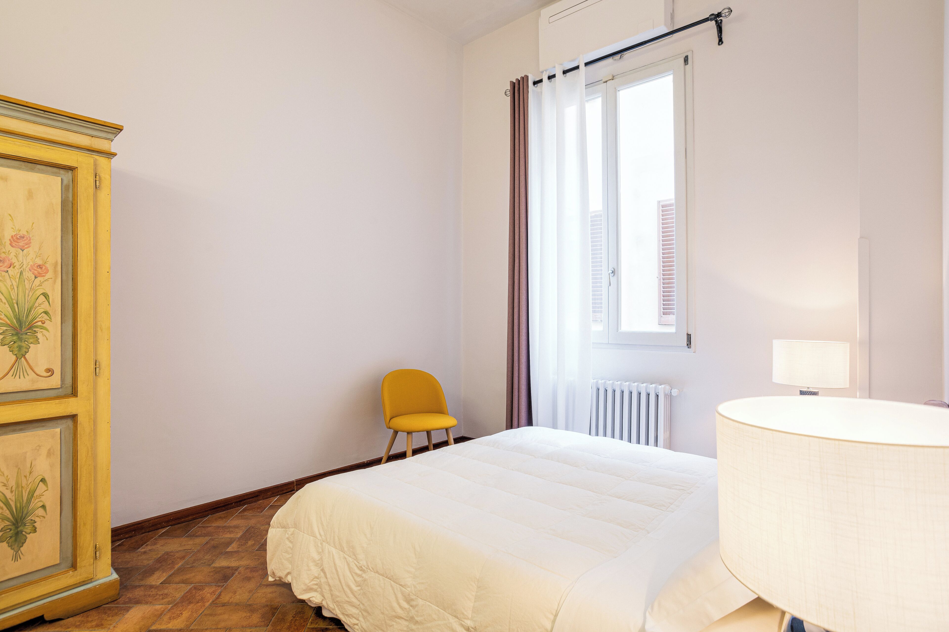 Een slaapkamer met een bed, een stoel, een lamp en een radiator.