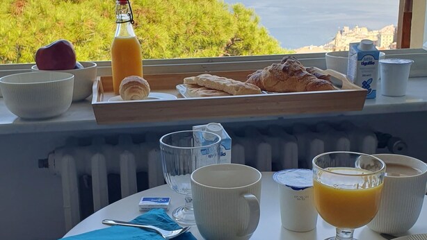Una mesa de desayuno con croissants, jugo y productos lácteos, con vistas a la costa.
