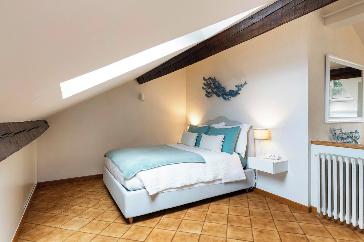 A bedroom with a bed, a bedside table, a lamp, a wall decoration, and a radiator.