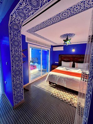A bedroom with a bed, a nightstand, a decorative ceiling light, and a view through a glass door to an outdoor area.