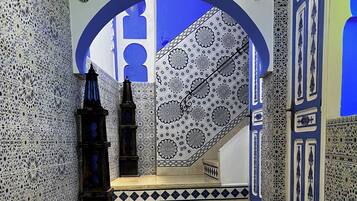 Un escalier recouvert de carreaux bleus et blancs formant un motif, menant à une pièce dont le mur est également décoré d’un motif bleu et blanc, et qui est éclairée par un luminaire en forme d’étoile.