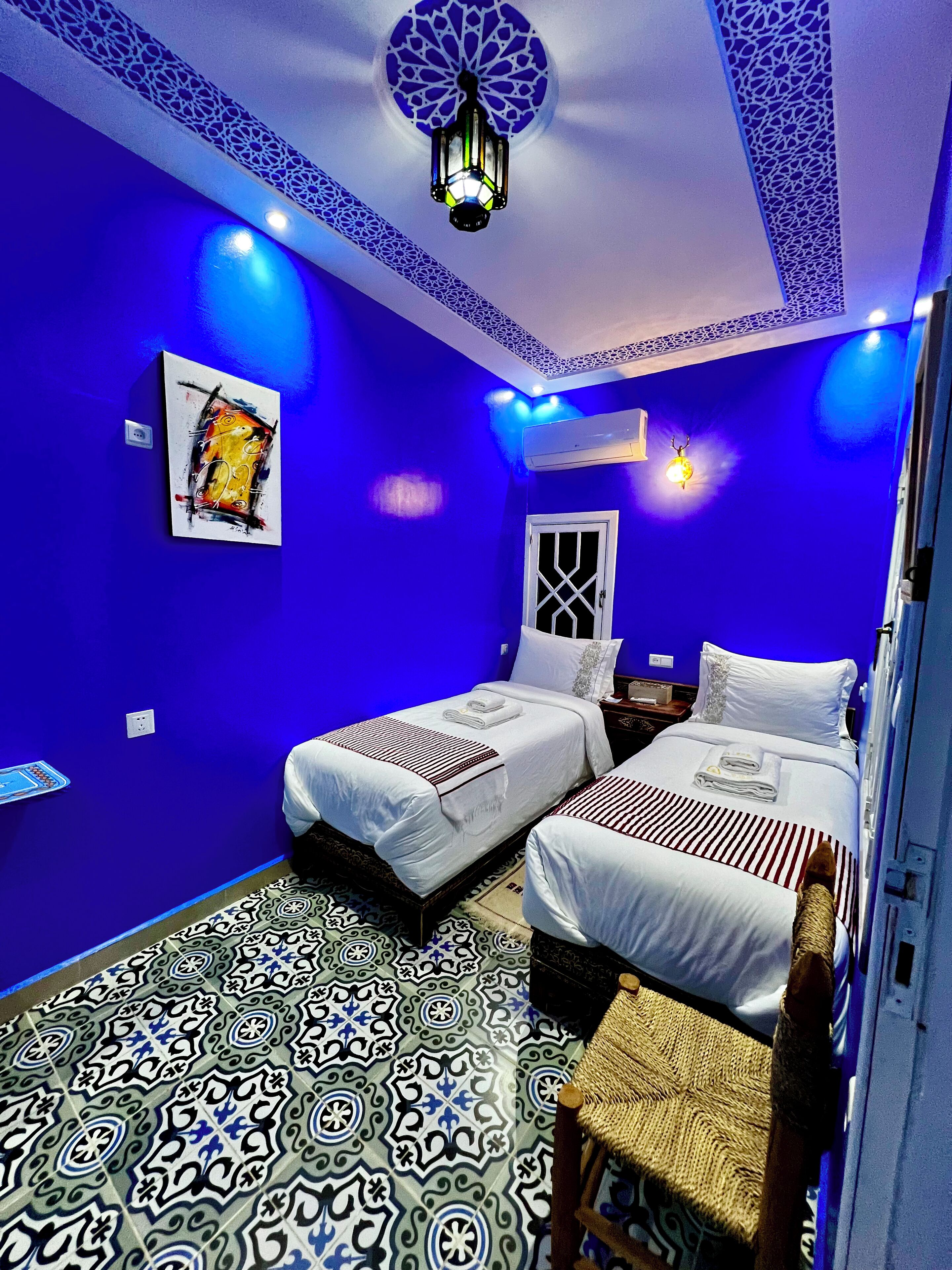 Une chambre avec deux lits, un sol à motifs et un luminaire décoratif au plafond.