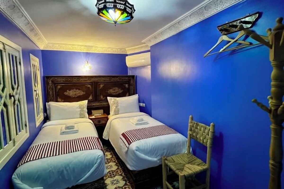 Una habitación con dos camas, cabecera de madera, un adorno en la pared y una lámpara de pared original.
