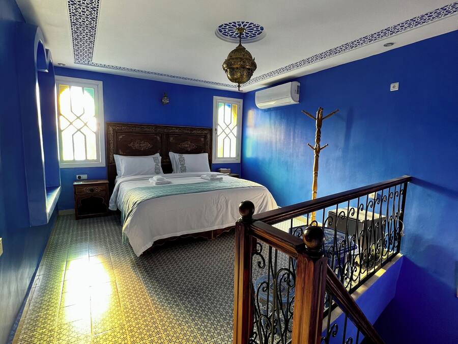 A bedroom with a bed, two bedside tables, a window, a ceiling fan, and a staircase with a railing.