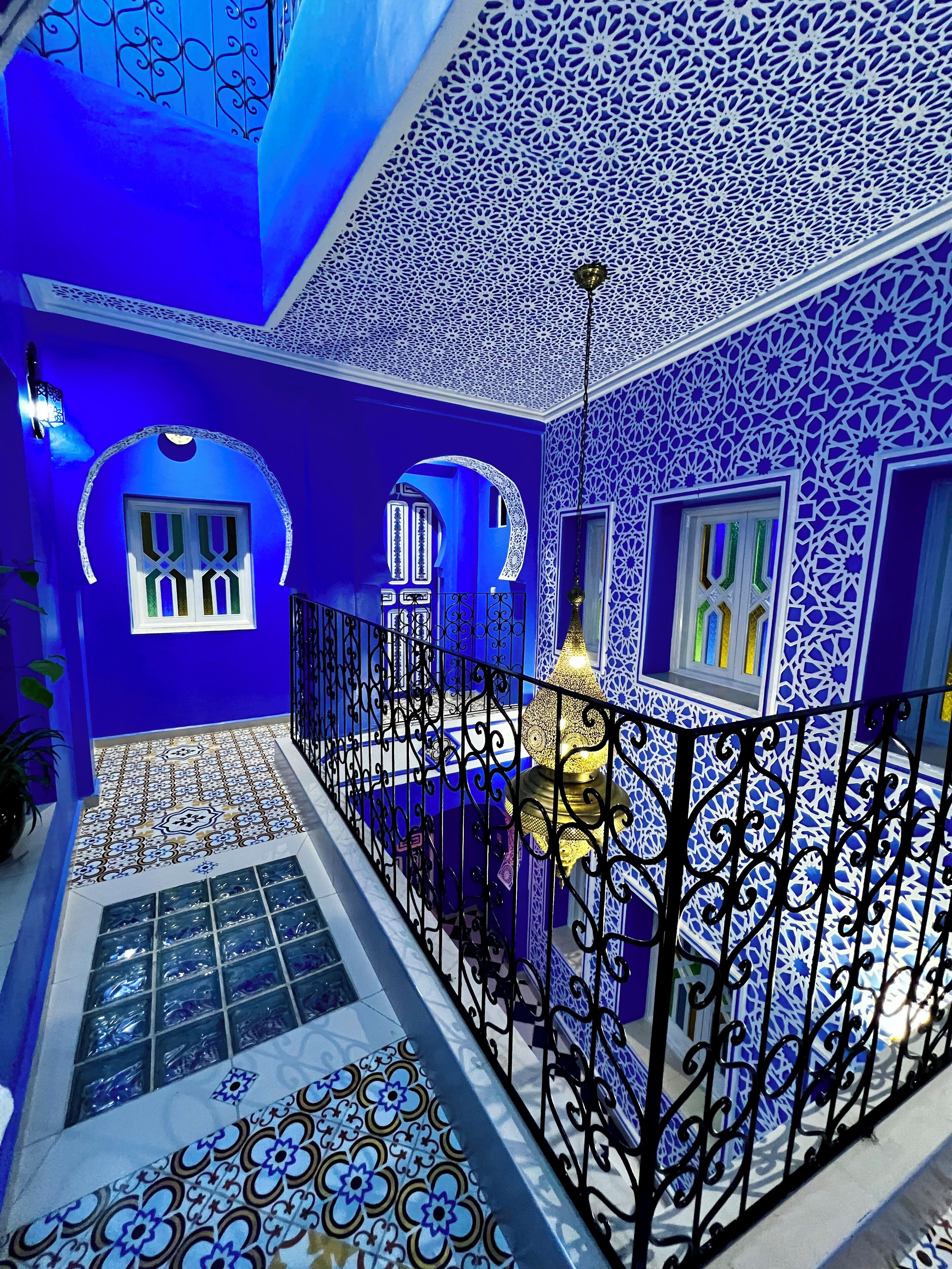 A blue-walled interior with ornate patterns, a balcony with a metal railing, and a decorative lamp.