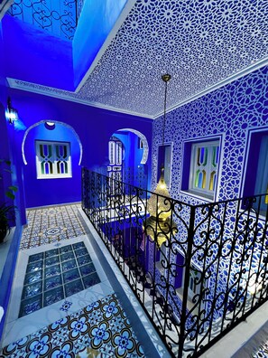 A blue-walled interior with ornate patterns, a balcony with a metal railing, and a decorative lamp.