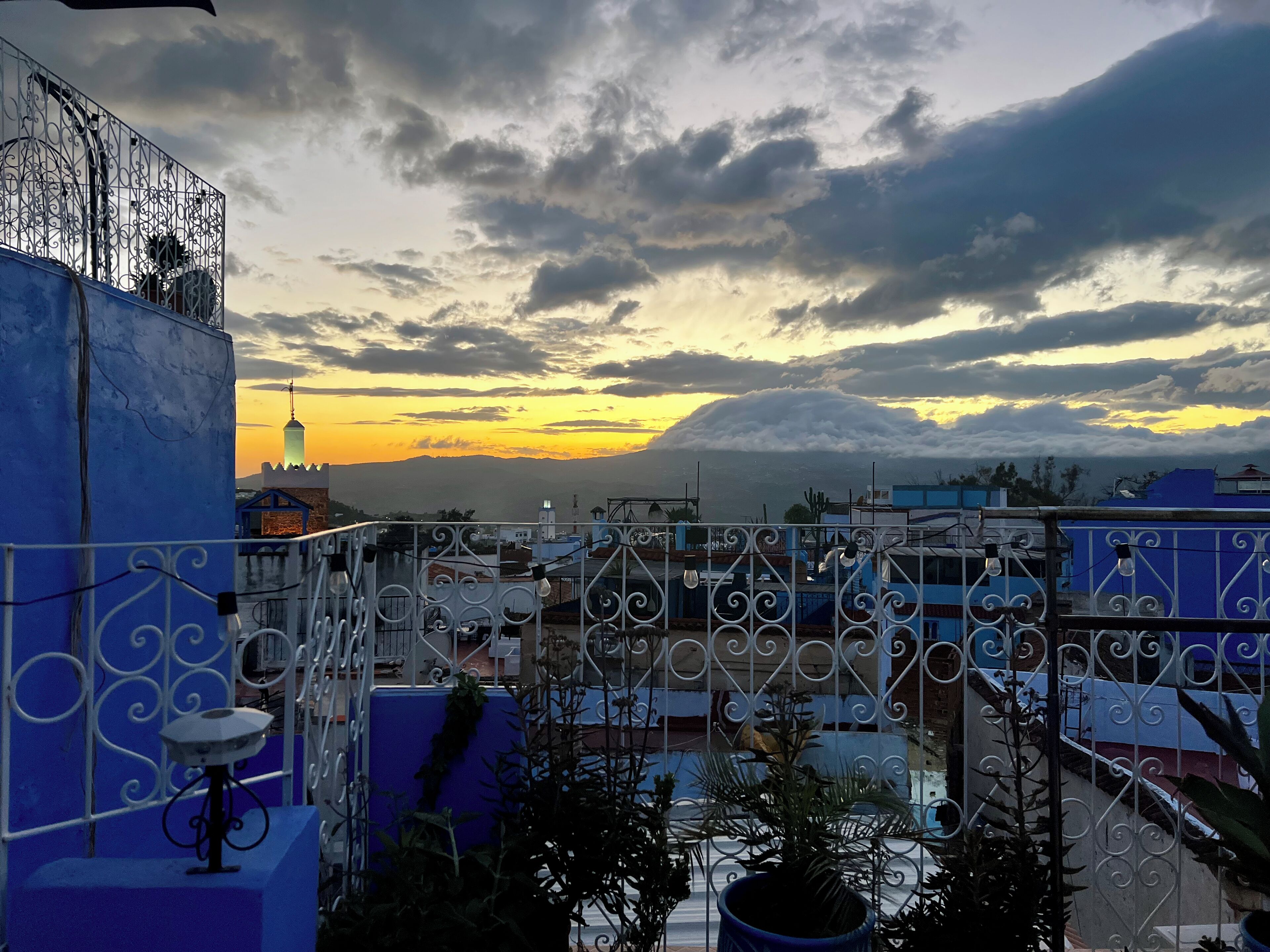 A rooftop view with a sunset, blue buildings, and a metal fence.