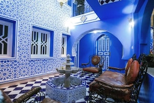 A traditional Moroccan interior with intricate tile work, a fountain, and a seating area.