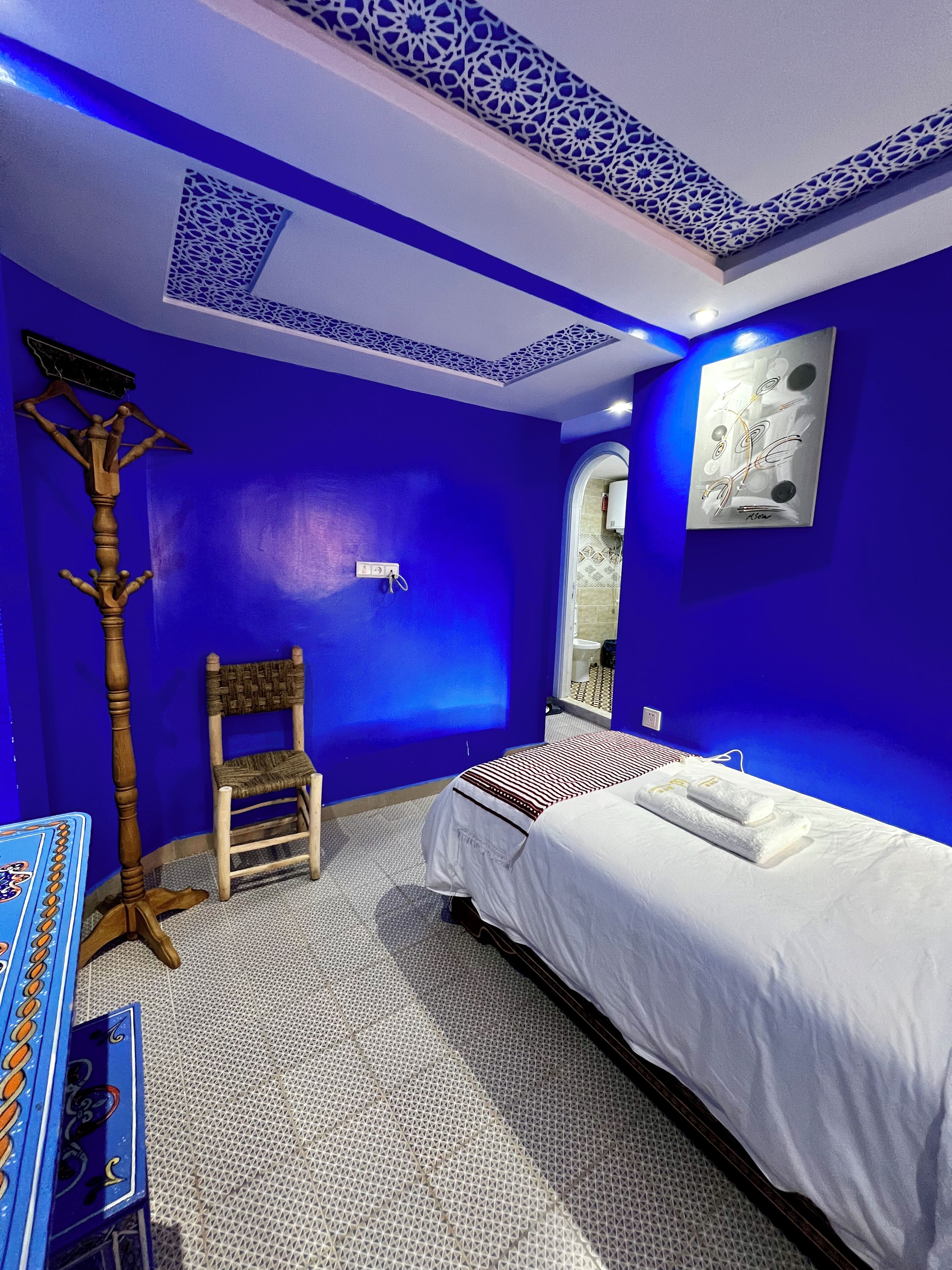 Une pièce aux murs bleus, un lit avec une literie blanche, une chaise en bois et un plafond décoratif.