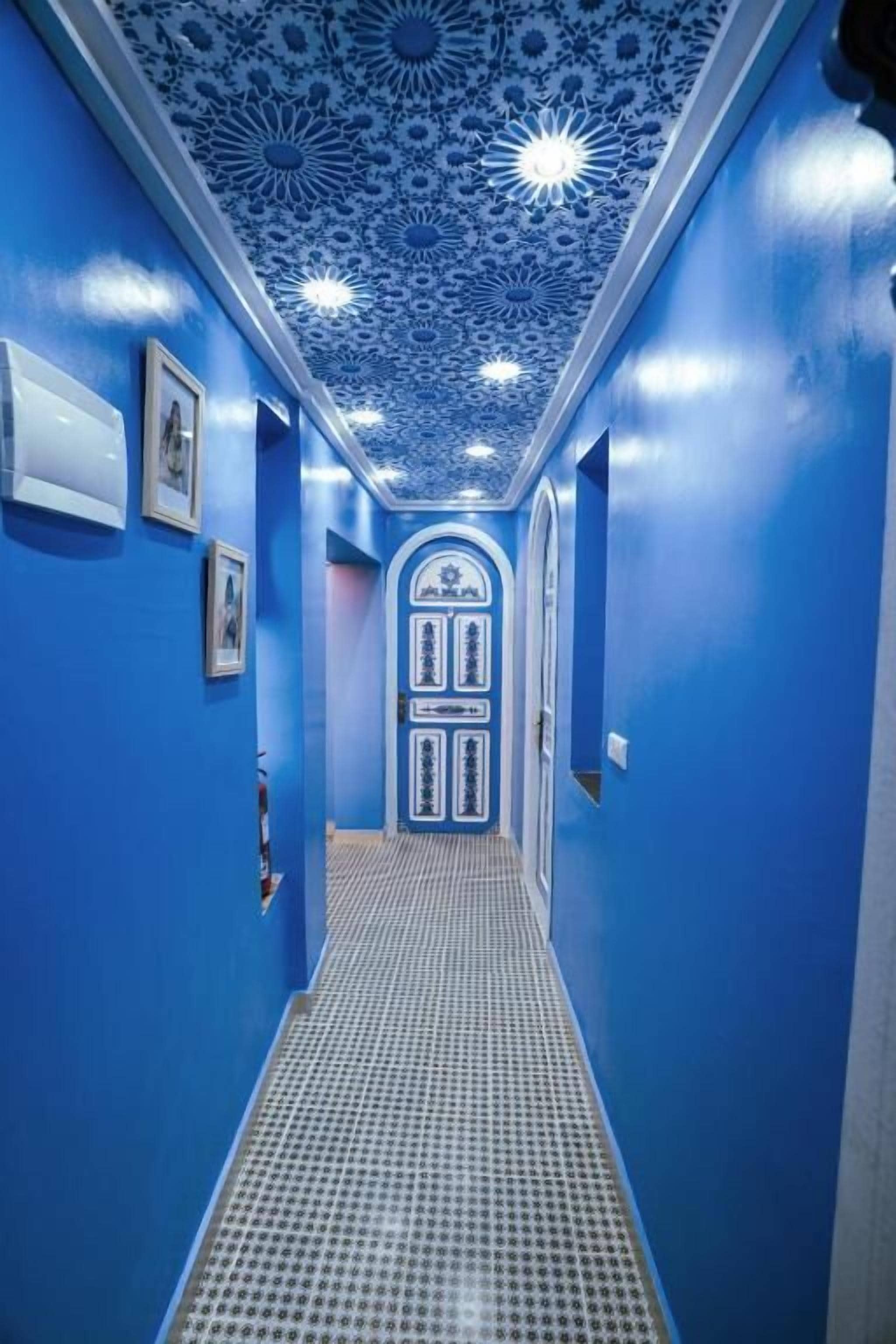 A hallway with blue walls and a patterned ceiling, leading to a door with decorative panels.