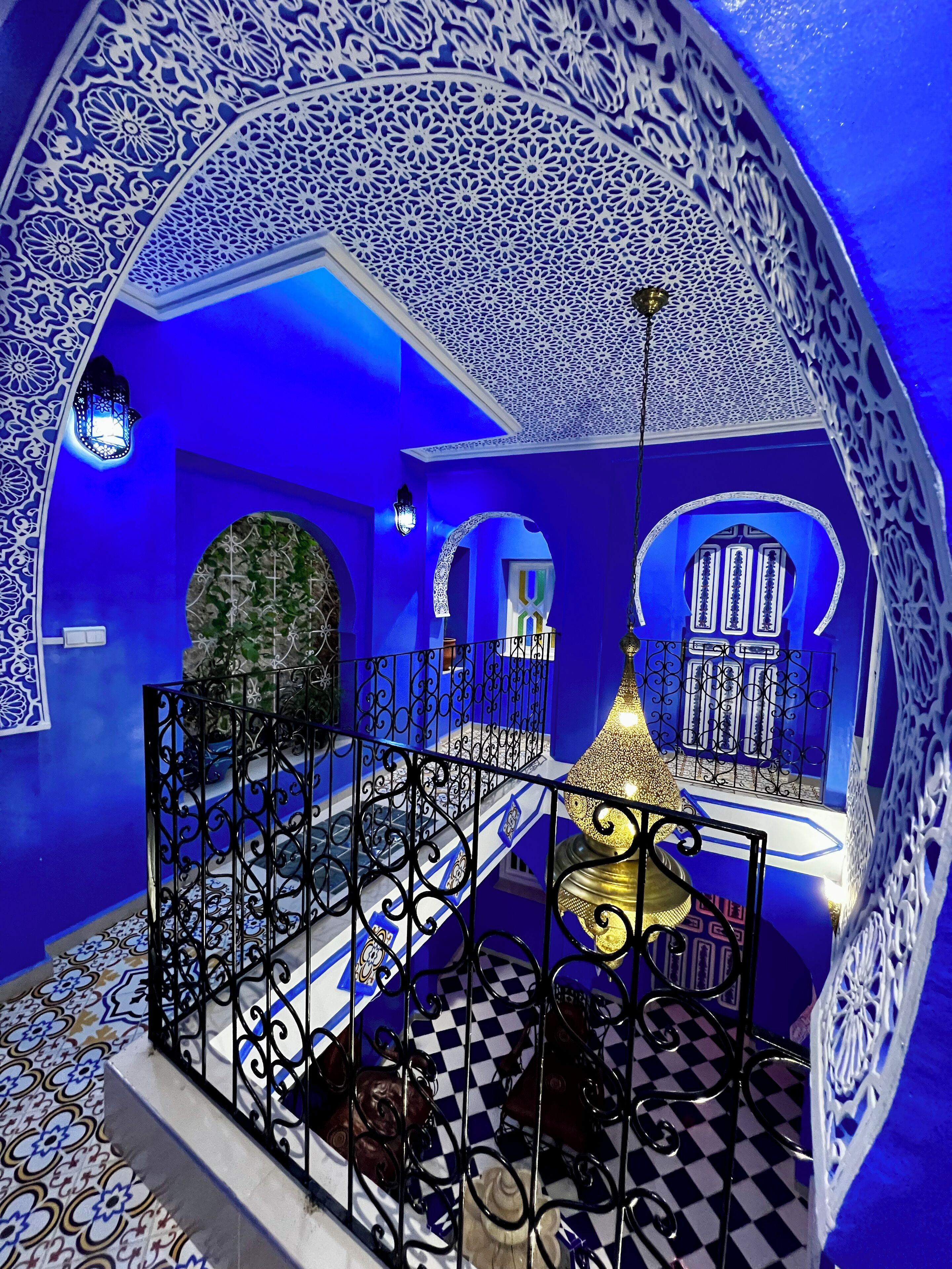 A blue-themed interior with ornate white patterns, a checkered floor, and a central chandelier.