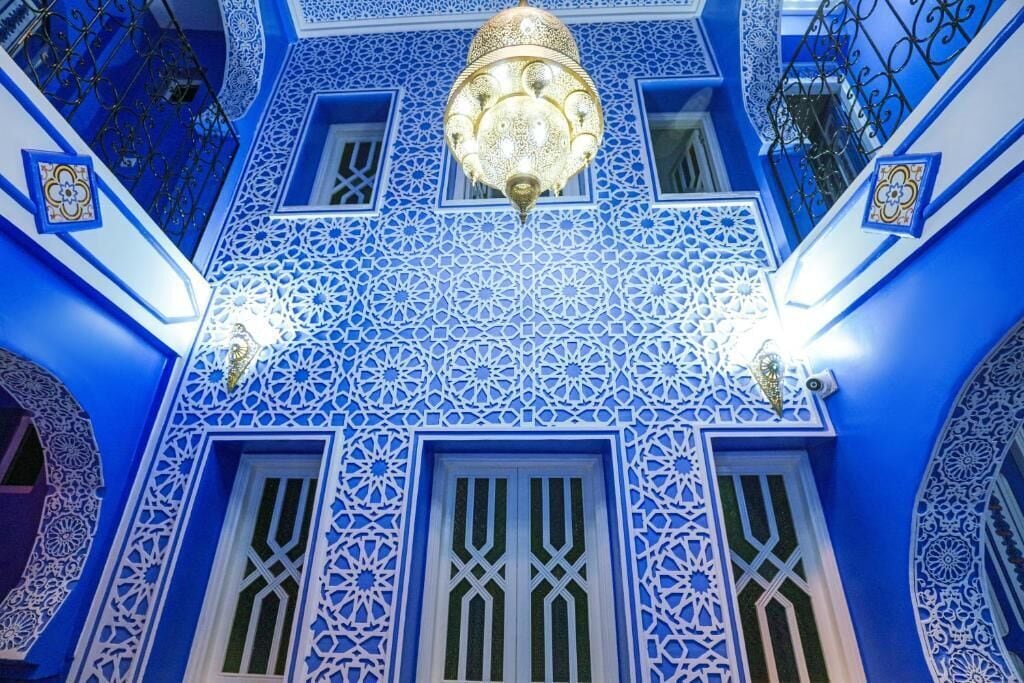 A room with intricate blue and white geometric patterns on the walls and ceiling, a chandelier, and a window with a unique design.